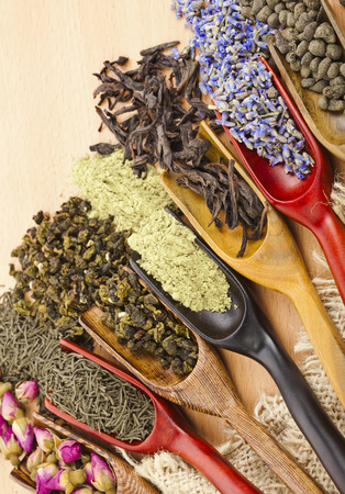 assortment of dry tea leaves and addition in spoon scoops close up on wooden table backgroundの写真素材