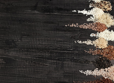 Border of colorful varieties whole grain rice in a rustic wooden surface backgroundの写真素材