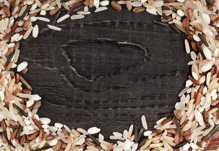 Frame made of colorful blend of rice varieties : brown rice, mixed wild rice, white (jasmine) rice in a rustic wooden surface backgroundの写真素材