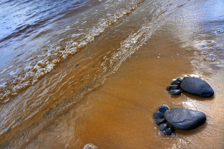 pair of feet made from pebbles on the sea sand texture surface backdropの写真素材