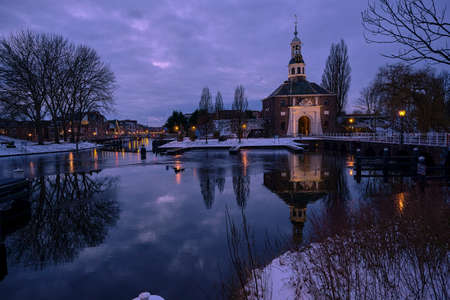 blue sky above the gate of the city of Leiden in winter with ice and snow by the canal in evening lightの写真素材