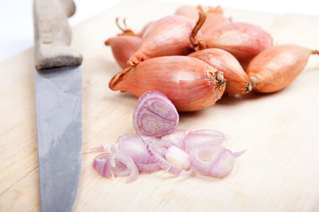 bunch of shallots with one sliced, old knife on wooden board, white backgroundの写真素材