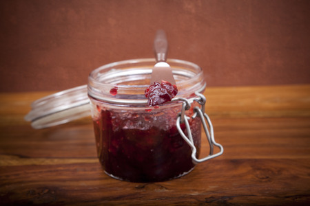 still life of cherry jam in transparent bowl on wooden table with rustic grunge background
