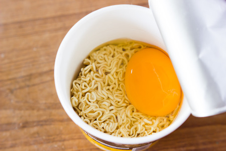 raw instant noodle in cup add egg on wood backgroundの写真素材