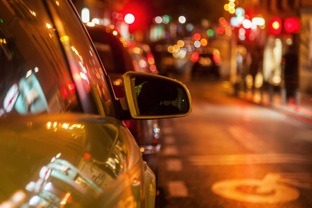 parked car on a city road at night with focus on the rear mirror and blurred background with colorful lightsの写真素材