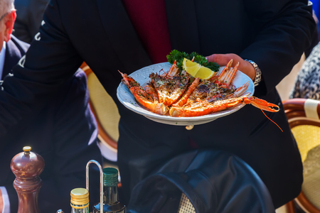 waiter serves a plate with lobster in an Italian outdoor restaurantの写真素材