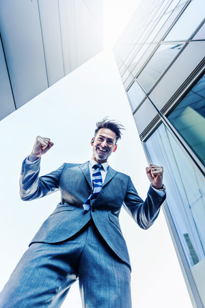 picture of a businessman who stands between skyscrapers and makes a winners fistの写真素材