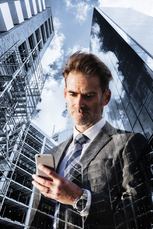 double exposure picture of a businessman with phone and skyscrapers with construction sitesの写真素材