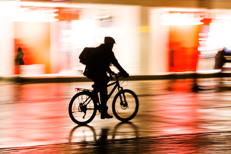 silhouette of a bicycle rider at night with camera made motion blurの写真素材