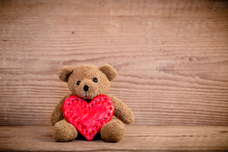 Teddy bear with heart sitting on old wood background.の写真素材