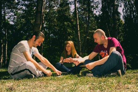 Three friend having fun by playing cards in the forestの写真素材