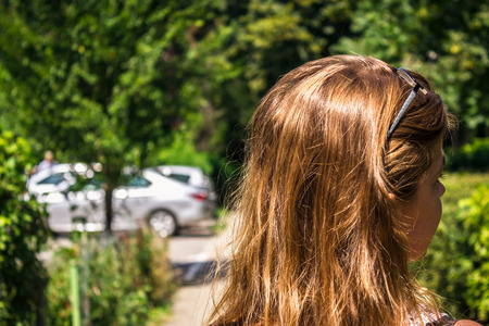 Girl with shiny hair walking on alley with a few cars in background in the summer. View from the backの写真素材