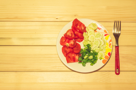 A few sliced vegetables on a plate next to a fork with a wooden backgroundの写真素材