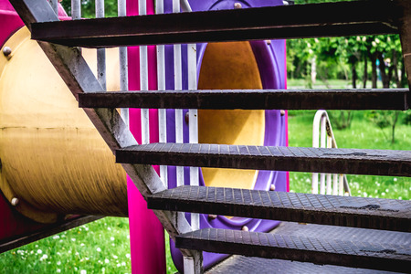 Shot made through the stairs of a slider from a kids playground with a tube to hide and trees and...