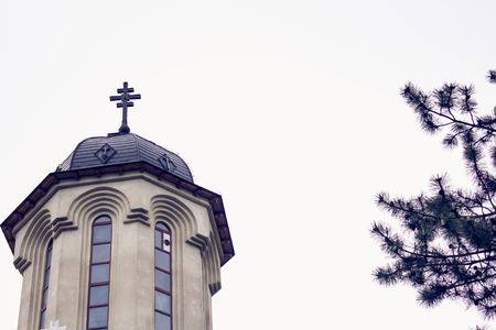 Shot of a church tower through some fir branches and trees on a cloudy dayの写真素材