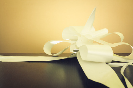 White beautiful bow on a dark wooden table with yellow backgroundの写真素材