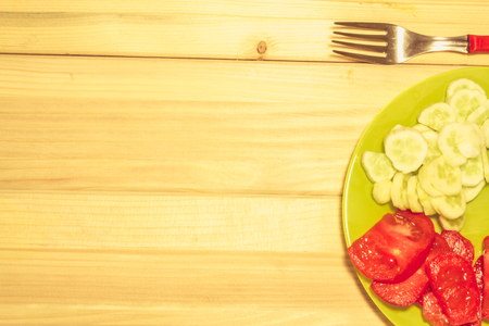 Close up shot to a few sliced vegetables on a plate next to a fork with a wooden backgroundの写真素材