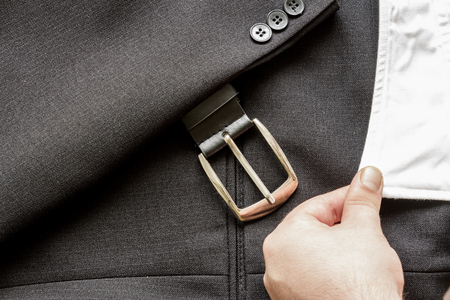 Hand holding a sleeve of a white shirt twith a few buttons on a business suit coat and leather beltの写真素材