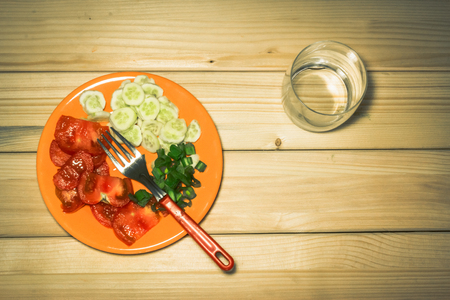 A few sliced vegetables on a plate next to a knife, an empty glass on a wooden backgroundの写真素材