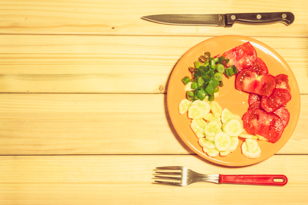 A few sliced vegetables on a plate next to a fork and a knife on a wooden backgroundの写真素材