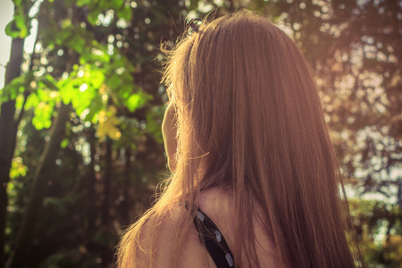 Girl in the forest standing in the sunlight with the face in to the sunの写真素材