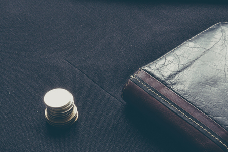 Close up of a business leather wallet near a stack of coins on a suit fabric as backgroundの写真素材