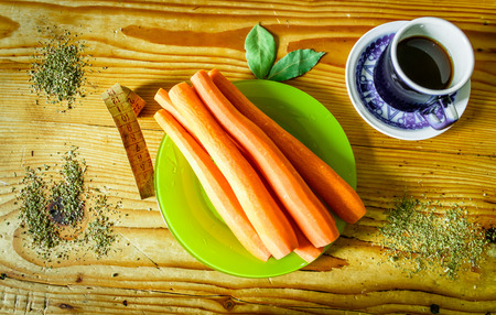 Carrot on a green plate sitting on a wood table salted with oregano next to a cup of coffee and two leafs of laurelの写真素材
