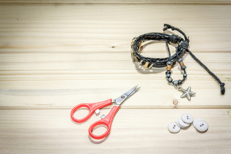 A leather bracelet, a pair of scissors and a few buttons on a wooden tableの写真素材
