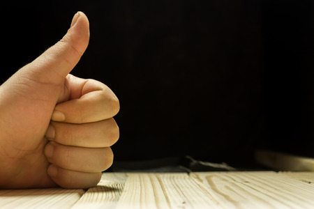 Hand showing the like symbol on a wooden tableの写真素材