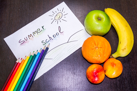 Summer tasty fruits on a dark background next to a note representing summer school and a few pencilsの写真素材