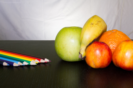 Summer tasty fruits on a dark background next to a few pencilsの写真素材