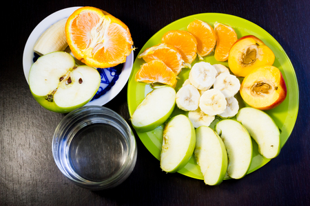 Summer tasty fruits on a few plates and a glass of water on a dark backgroundの写真素材
