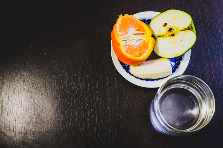 Summer tasty fruits on a plate and a dark background next to a glass of waterの写真素材