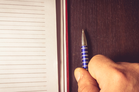 Close up shot to a hand holding a pen next to an agenda on a wooden backgroundの写真素材