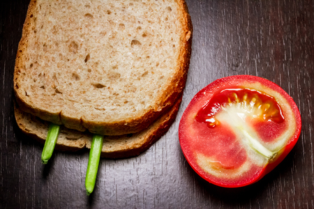 Close up shot to a simple sandwich next to a sliced tomato on a dark wooden backgroundの写真素材