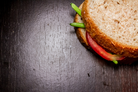 Close up shot to a simple sandwich made from a few green onion leafs and a slice of tomato on a wooden backgroundの写真素材