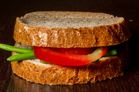 Close up shot to a simple sandwich made from a few green onion leafs and a slice of tomato on a wooden backgroundの写真素材