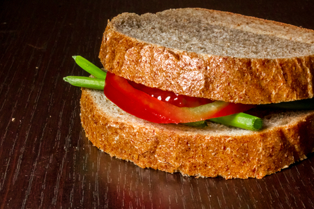 Close up shot to a simple sandwich made from a few green onion leafs and a slice of tomato on a wooden backgroundの写真素材