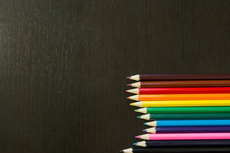 Well arranges colored pencils in order to form rainbow colors on a dark wooden backroundの写真素材