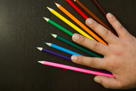 Well arranges colored pencils in order to form rainbow colors on a dark wooden backround with a hand covering themの写真素材