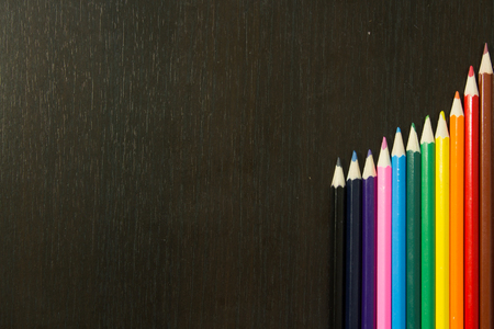 Well arranges colored pencils in order to form rainbow colors on a dark wooden backroundの写真素材