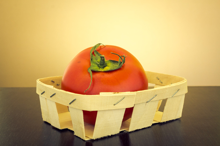 Tomato in an handmade little basket made from wood on a dark wooden table with yellow backgroundの写真素材