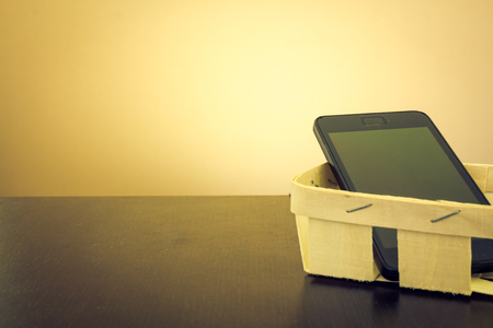 A smartphone in an handmade little basket made from wood on a dark wooden table with yellow backgroundの写真素材