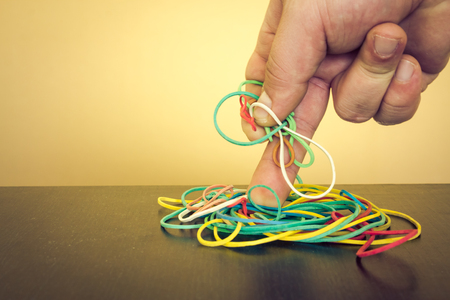 Hand taking a few colored elastic rubbers from a dark wooden table with yellow backgroundの写真素材
