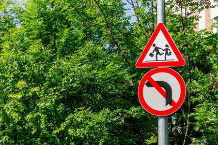 Shot to a couple of traffic sign indicating to pay attention to kids and being forbidden to turn to leftの写真素材