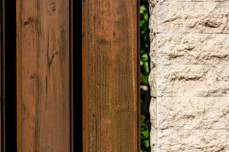 Close up shot to a fence made from a few dark wooden planks and som rocky bricksの写真素材