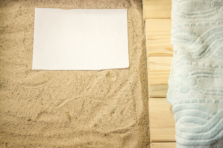 Shot to a few wooden planks, sand, a few summer clothing articles and a white plain piece of paperの写真素材