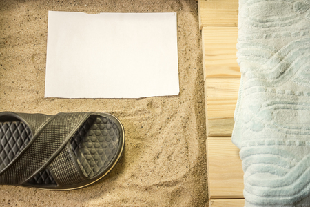 Shot to a few wooden planks, sand, a few summer clothing articles and a white plain piece of paperの写真素材