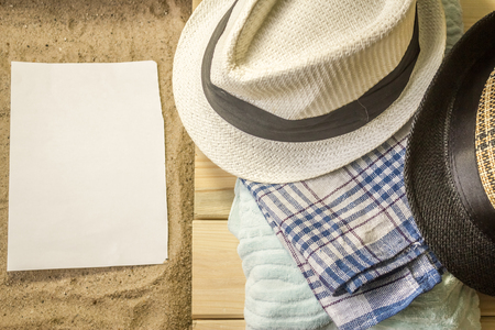 Shot to a few wooden planks, sand, a few summer clothing articles and a white plain piece of paperの写真素材