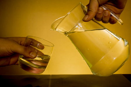 Elegant shot of two hands preparing to pour some water from a pitcher into a glass on a dark backgroundの写真素材